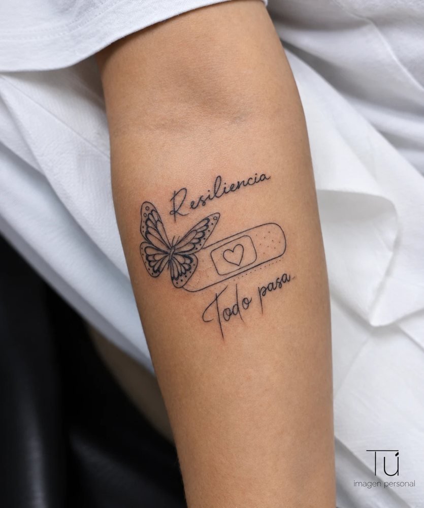 Tatuaje de línea fina con mariposa, tirita y la frase Resiliencia, todo pasa